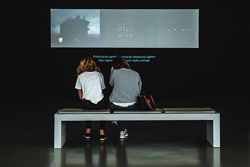 Two people sitting on a bench looking at a screen.